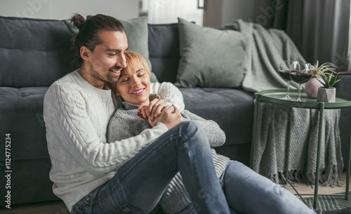 Canvas Print A happy couple in cozy sweaters is relaxing and cuddling at home on the living room floor, enjoying quality time together