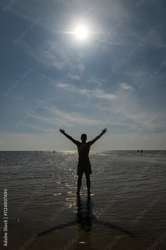 © Milou Dirks - silhouette of a happy man in shorts standing on the beach in the blue ocean with arms wide open and sun above