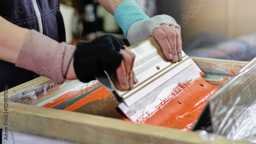 male hands with a squeegee. silk screen textile printery. manual screen printing. creating print on t-shirt