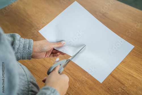 Woman hands cutting paper with scissors on a wooden table