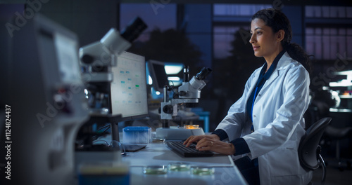 Hispanic Female Scientist Working on a Computer in the Evening. Specialist Using a Gene Sequencing Online Software. Advanced Biotechnology Lab in a Medical Research and Development Center