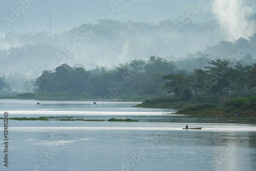 A fisherman skillfully casts a net from a small wooden boat on a tranquil lake, capturing the harmony between human livelihood and nature.