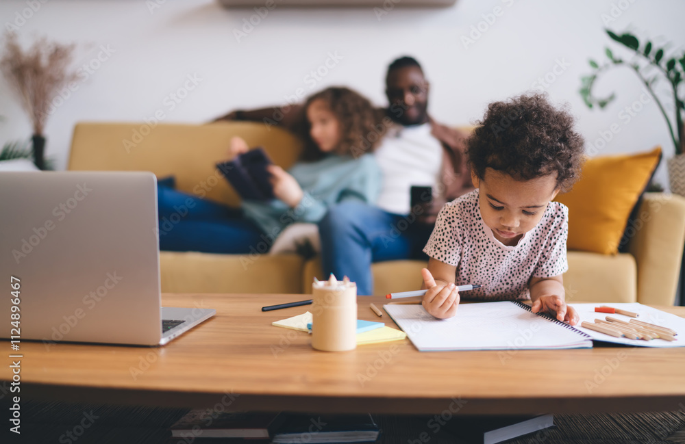 Modern family balancing digital and traditional learning at home interior, Young child focused on drawing while blurred parents relaxes in background in contemporary living space with natural light Modern family balancing digital and traditional learning at home interior, Young child focused on drawing while blurred parents relaxes in background in contemporary living space with natural light