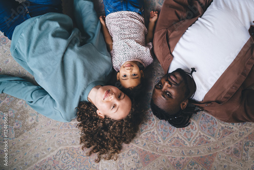 Half length lifestyle portrait of diverse family looking at camera while lying at floor, Young child centered between parents capturing essence of unity and unconditional love emotional connection photo