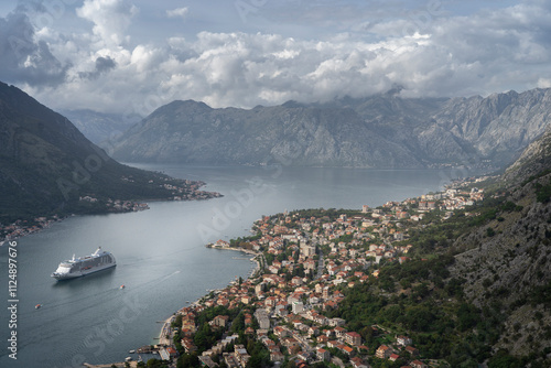 the new part of the Kotor city illuminated by the rays of sun, and the bay surrounded by mountains covered with clouds. In addition, the majestic cruise ship bringing thousands of tourists to Kotor