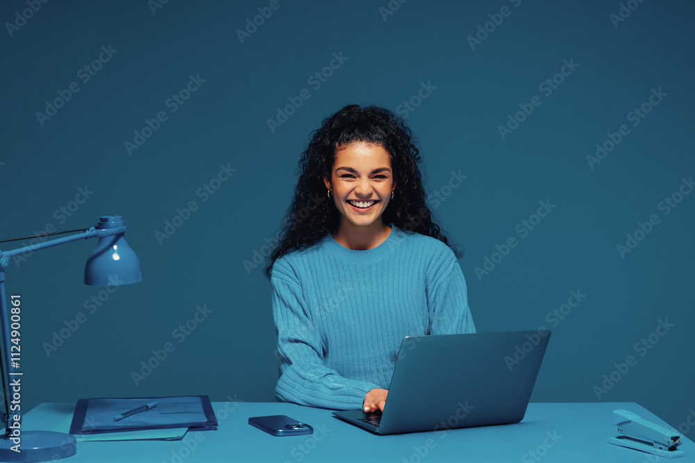 © Jacob Lund - Smiling multiracial woman sitting at desk with laptop in monochromatic office