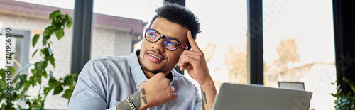 Handsome man contemplates solutions at his desk surrounded by vibrant plants and natural light.