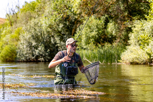 Фототапет Man catching fish while fly fishing in a river