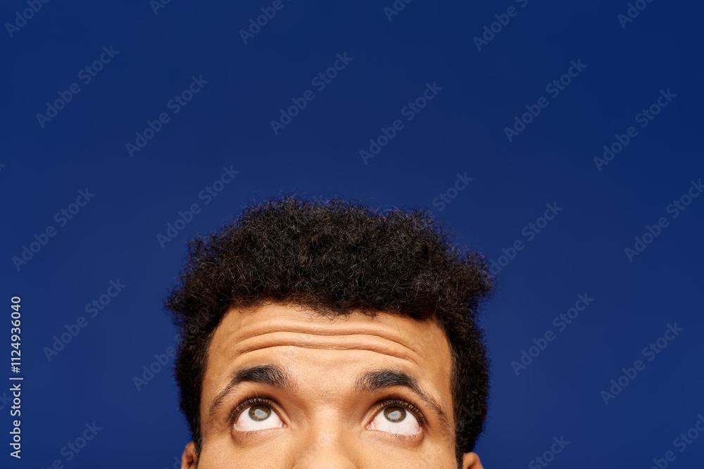 Obraz premium A handsome man looks thoughtfully upwards, his expression hinting at curiosity and wonder.