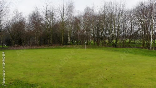 Aerial drone footage of a golf course green in the winter time showing bare trees around the golfing course on a cold winters day