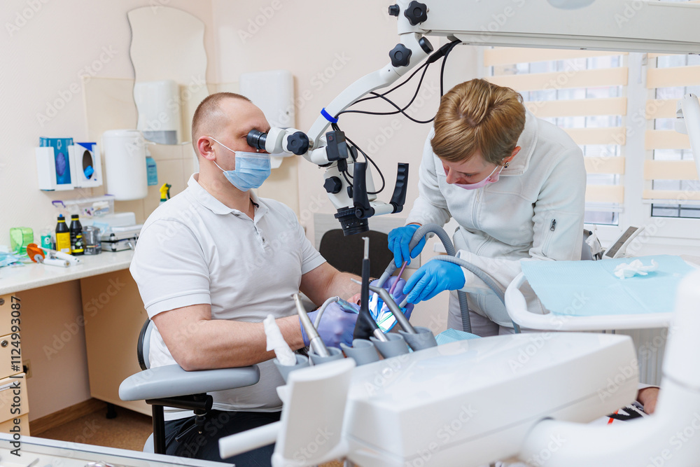 Fototapeta premium The dentist is in his dental office. A dentist in a white uniform treats a patient's teeth with a dental microscope. Dental office