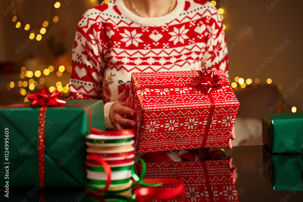 custom made wallpaper toronto digitalWoman wearing Christmas sweater holding wrapped Christmas gift with wrapping paper and ribbon table. Preparing presents for winter holidays