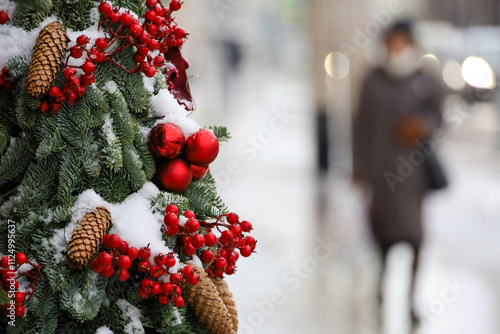 New Year celebration in city, snow covered Christmas tree branches with red balls on a street on walking people background photo