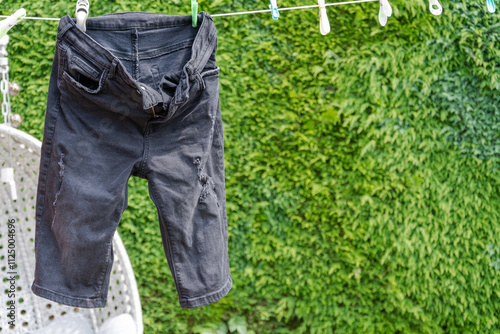 A pair of faded black denim, half-length shorts hang on a washing line.