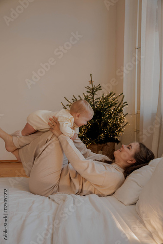 Mother with child on bed against Christmas tree, light vertical photo