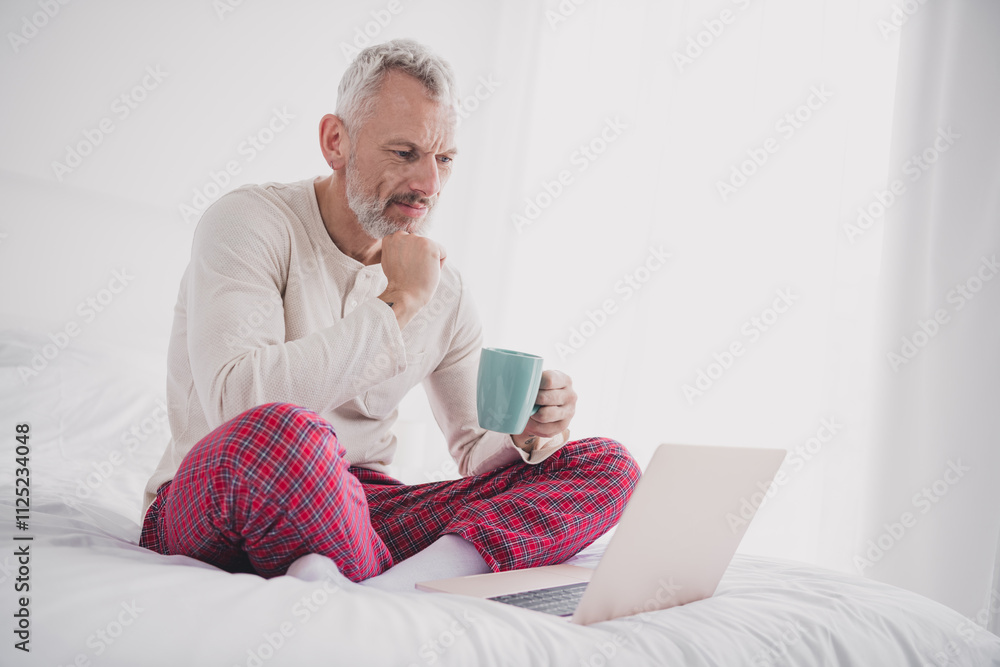 Mature man enjoying a relaxed morning on bed with coffee and laptop in cozy pajamas Mature man enjoying a relaxed morning on bed with coffee and laptop in cozy pajamas