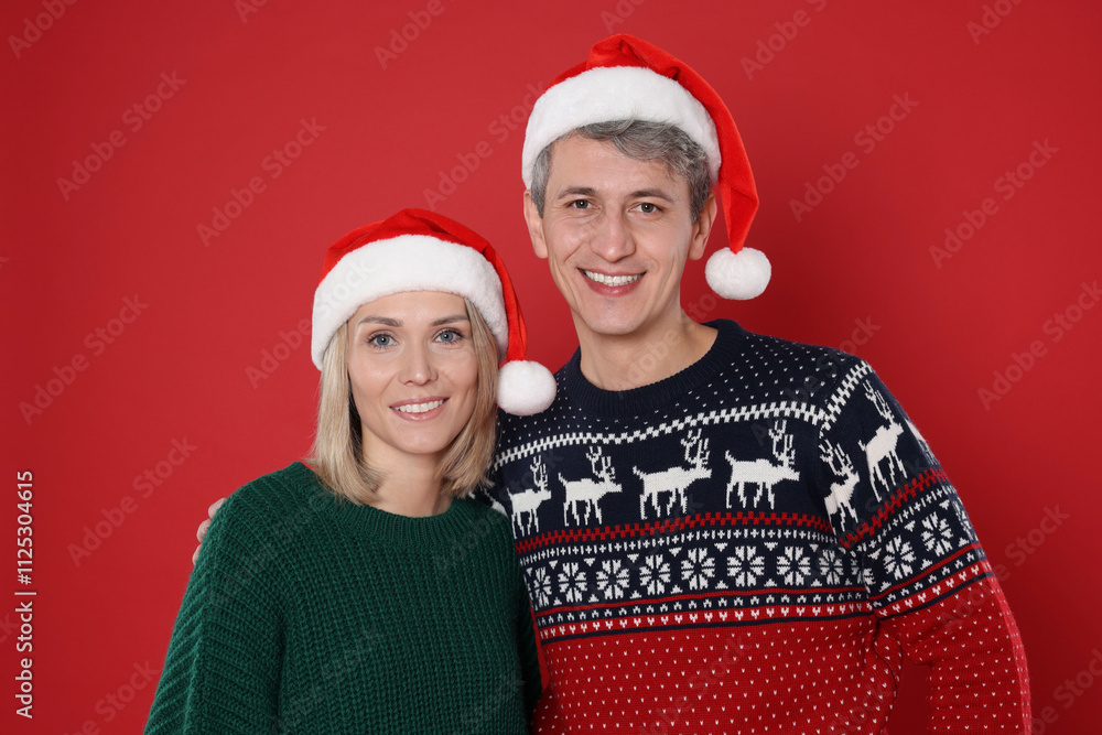Happy couple in Santa hats on red background. Christmas celebration Happy couple in Santa hats on red background. Christmas celebration