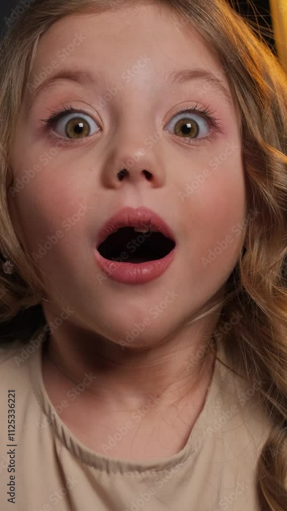 The little girl is surprised. Close-up portrait in the studio on a dark background. The little girl is surprised. Close-up portrait in the studio on a dark background.