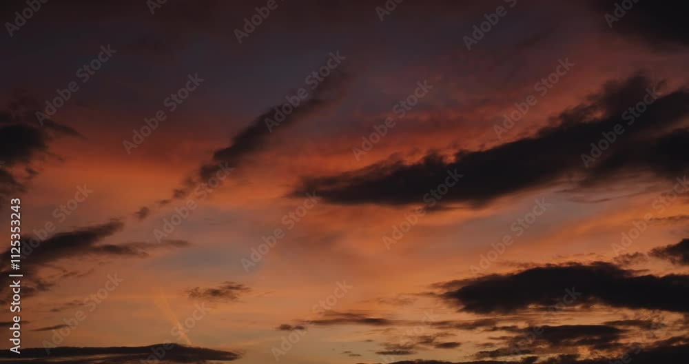 Timelapse of the sky after sunset with upper layer of clouds colored pink, orange and red by the hidden sun and lower streaks of dark clouds slowly coming and covering the view