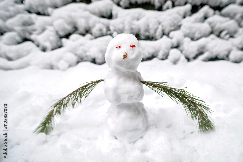 Obraz premium Small snowman made with fresh snow and pine branch arms on frosty day in winter setting. Handmade snowman with red eyes made of barberries fruits and nose made of pine cone. Snow-covered outdoor scene