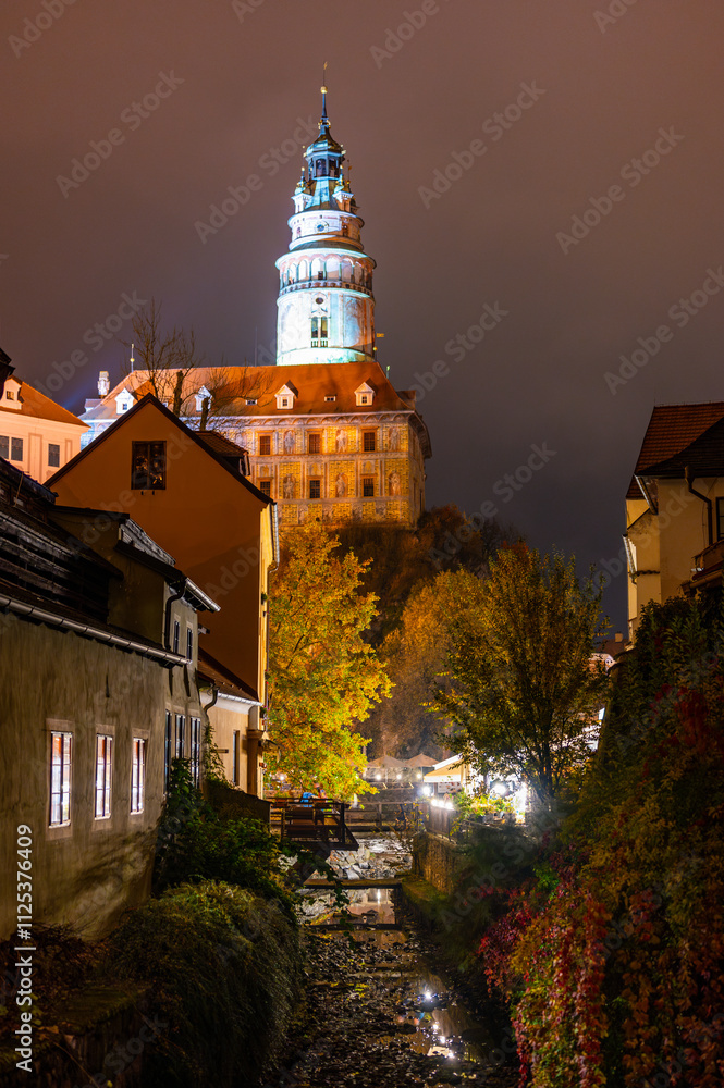 A stunning night view of the illuminated tower of Cesky Krumlov Castle towering above the Vltava River, creating a magical atmosphere with the reflection in the water