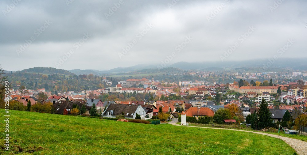A panoramic view of Cesky Krumlov on an overcast autumn day, showcasing the town's historic rooftops, winding Vltava River, and iconic castle tower under a dramatic cloudy sky
