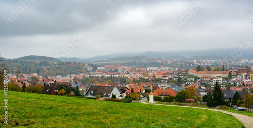 Obraz na płótnie A panoramic view of Cesky Krumlov on an overcast autumn day, showcasing the town's historic rooftops, winding Vltava River, and iconic castle tower under a dramatic cloudy sky w salonie