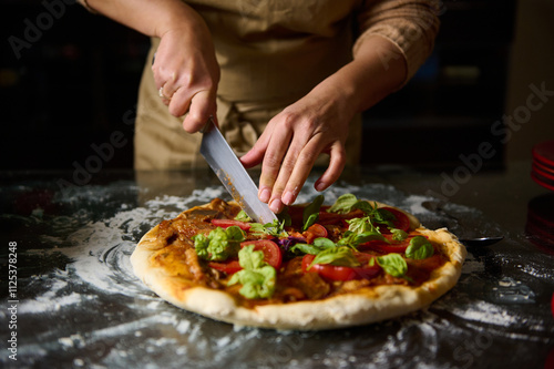 Chef slicing freshly baked pizza with toppings in kitchen