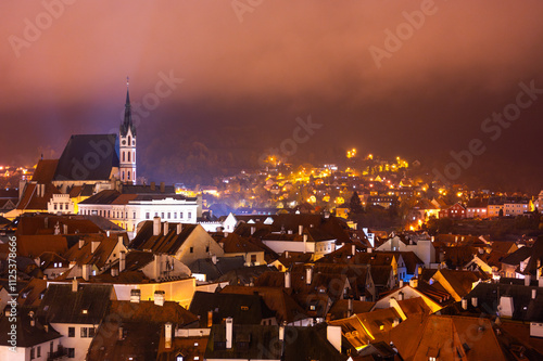 Obraz na płótnie A panoramic night view of Cesky Krumlov, showcasing the rooftops, illuminated buildings, and the Church of St. Vitus beautifully lit up against the dark sky w salonie