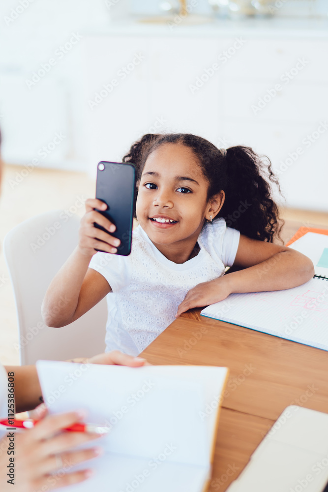 Daughter taking picture of mother while looking at camera studying at home together Daughter taking picture of mother while looking at camera studying at home together