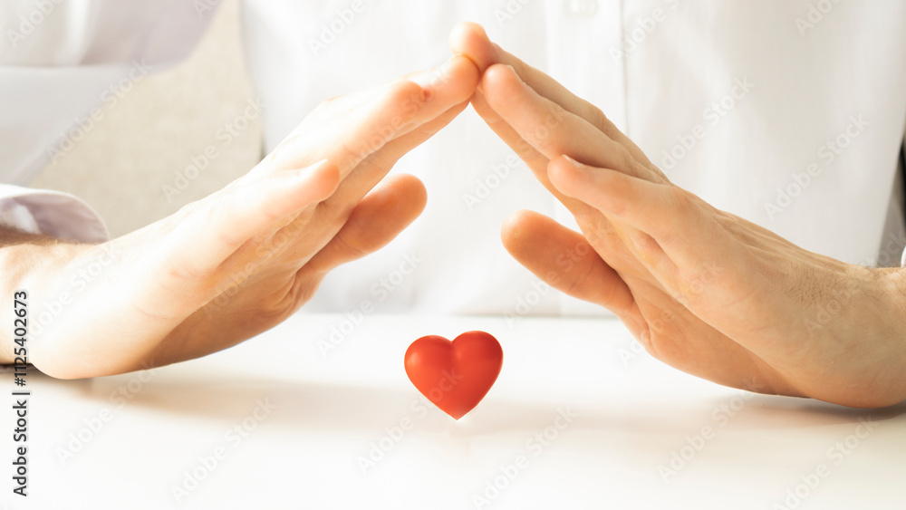 Fototapeta premium Cropped photo of a man making a roof over a small heart on a table.
