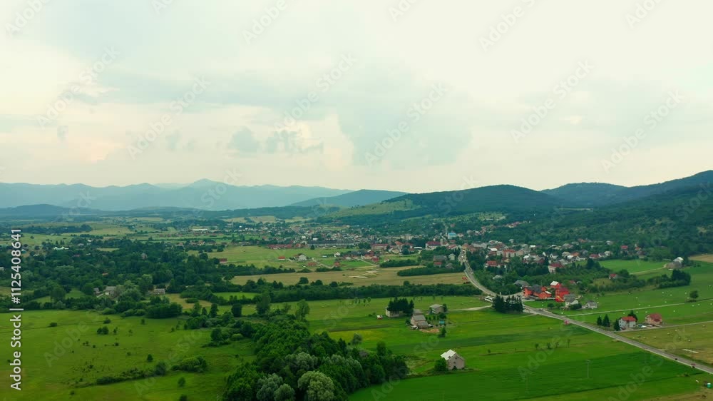 A town in a picturesque valley at the foot of the mountains. Fields and meadows for haymaking and grazing. The foothill and mountain-plain landscape of the town of Korenica in Croatia. A town in a picturesque valley at the foot of the mountains. Fields and meadows for haymaking and grazing. The foothill and mountain-plain landscape of the town of Korenica in Croatia.