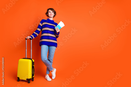 Full body length photo of young tourist girl in pullover and jeans holding tickets abroad dreaming about vacation isolated on orange color background photo