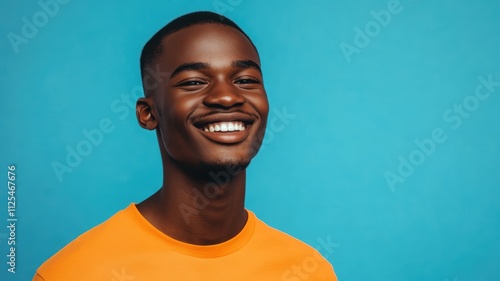 Happy young African man with a shaved head dressed in a bright orange shirt standing against a solid blue background