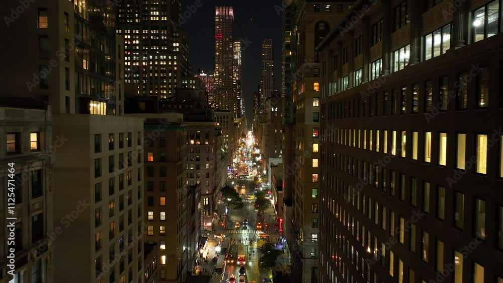 Cars drive on a busy Midtown Manhattan street in New York City at night. Apartment windows illuminated, pedestrians walk and men work outdoor Cars drive on a busy Midtown Manhattan street in New York City at night. Apartment windows illuminated, pedestrians walk and men work outdoor