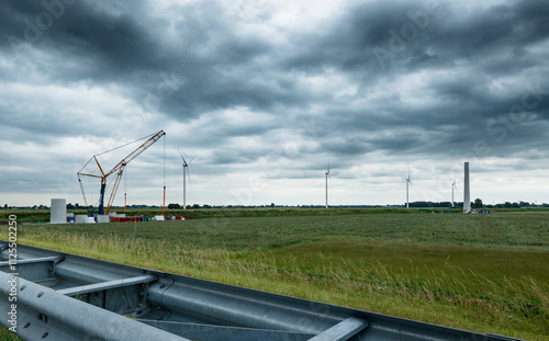 Wind farm construction site under a cloudy sky.  Heavy machinery and  concrete structures visible.  Rural landscape. photo