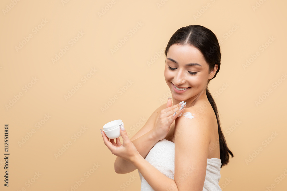 A young woman with brunette hair applies moisturizer to her shoulder, smiling happily. She is in a calm, isolated environment, focused on her skincare ritual for pampering and self-care, copy space A young woman with brunette hair applies moisturizer to her shoulder, smiling happily. She is in a calm, isolated environment, focused on her skincare ritual for pampering and self-care, copy space