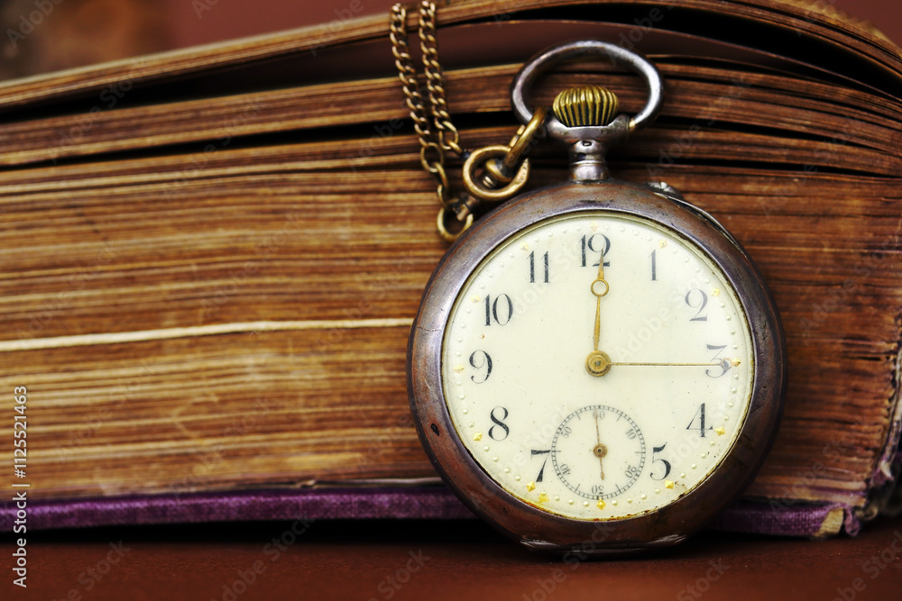 Eine antike Taschenuhr lehnt an einem alten Buch mit vergilbten Seiten
Eine antike Taschenuhr lehnt an einem alten Buch mit vergilbten Seiten