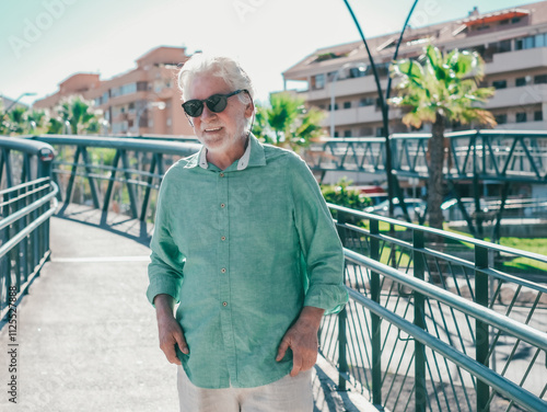 Senior bearded man walks on a modern pedestrian bridge in an urban environment wearing casual clothes and walks with confidence, reflecting independence and positivity #1125527888