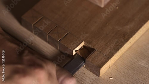 Close-up of a carpenter chiseling a mortise in wood for a multiple mortise and tenon joint. This detailed footage showcases the precision and craftsmanship involved in traditional woodworking