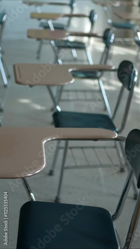 Vertical video desks in empty dark high, middle, or elementary school classroom with light coming through windows.