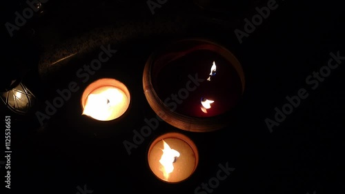 A clay candle burning at night on a grave. The candle's flame flutters in the wind.