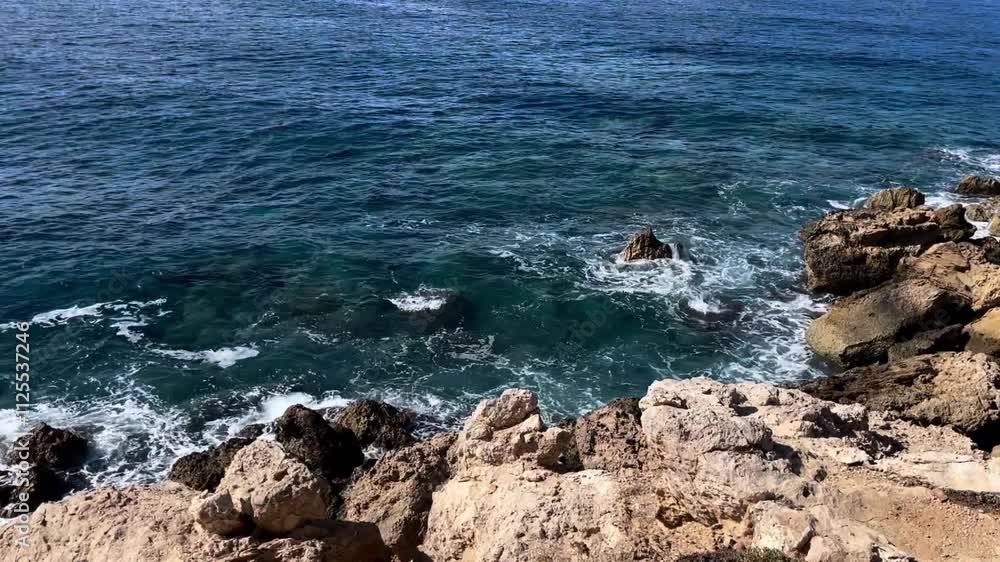 Horizontal daytime video of the Mediterranean Sea coast, blue waves atmospherically beating large brown light and dark rocks of beautiful Cyprus, sunlight shimmering rocks and waves colorful colors
