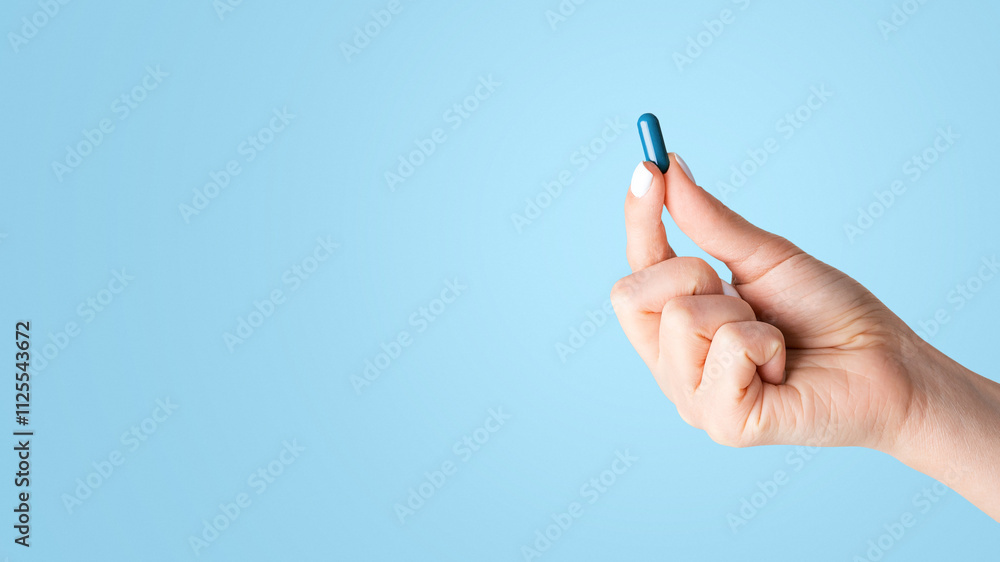 Unrecognizable young girl showing one blue pill over white background, closeup. Panorama Unrecognizable young girl showing one blue pill over white background, closeup. Panorama