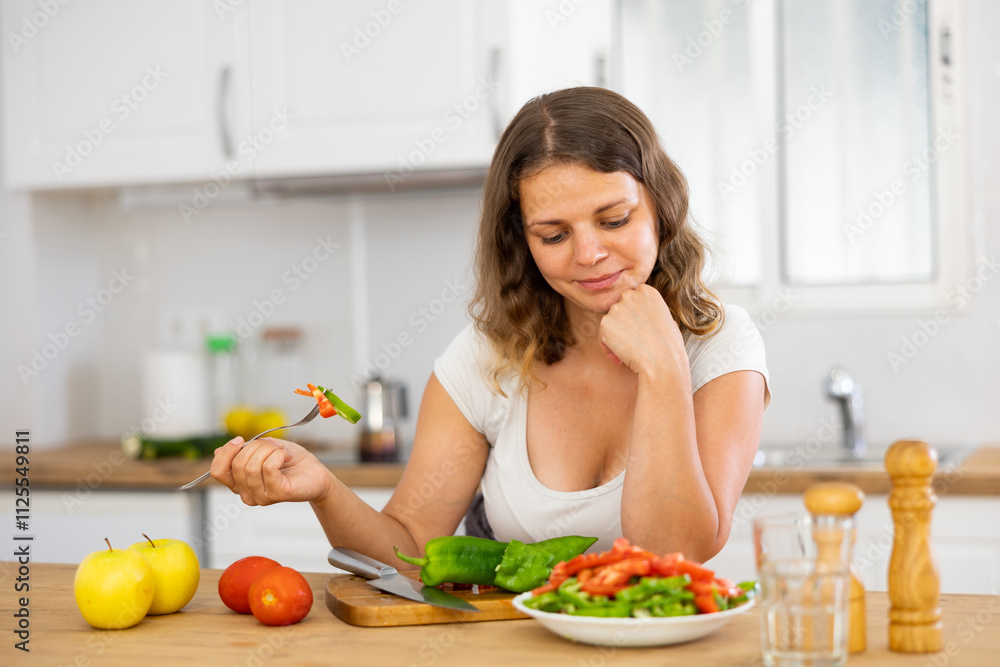 Positive young woman eating freshly made vegetarian salad at kitchen countertop Positive young woman eating freshly made vegetarian salad at kitchen countertop