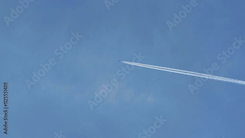 An airplane crosses a clear blue sky, leaving behind a white contrail that gradually dissipates. The smoke fades over time, creating a beautiful atmospheric effect