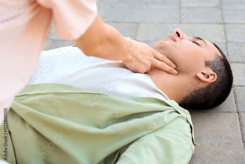 Young woman checking pulse of unconscious man having heart attack on street, closeup