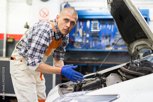 Car mechanic looking at open car hood for internal checking to maintenance vehicle in workshop