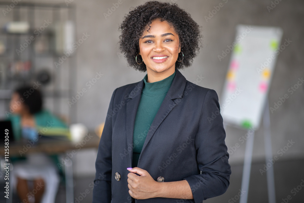 © Prostock-studio - A professional woman stands confidently in a contemporary office, showcasing teamwork and cooperation. Colleagues engage in productive discussions, thriving in a dynamic corporate environment.