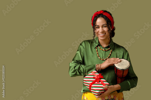 Young African-American woman with tam-tam drum and gift on green background. Kwanzaa celebration